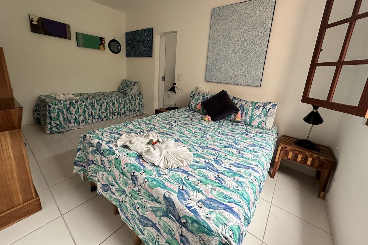 A bedroom with a large bed, a smaller bed, a nightstand, a lamp, and artwork on the walls.
