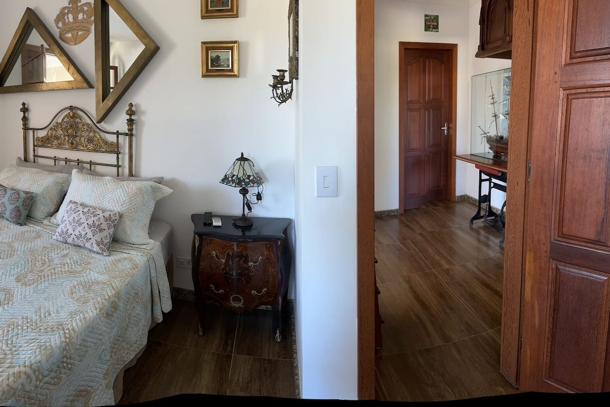 A bedroom with a bed, a chair, a small table, and a window with an open shutter.