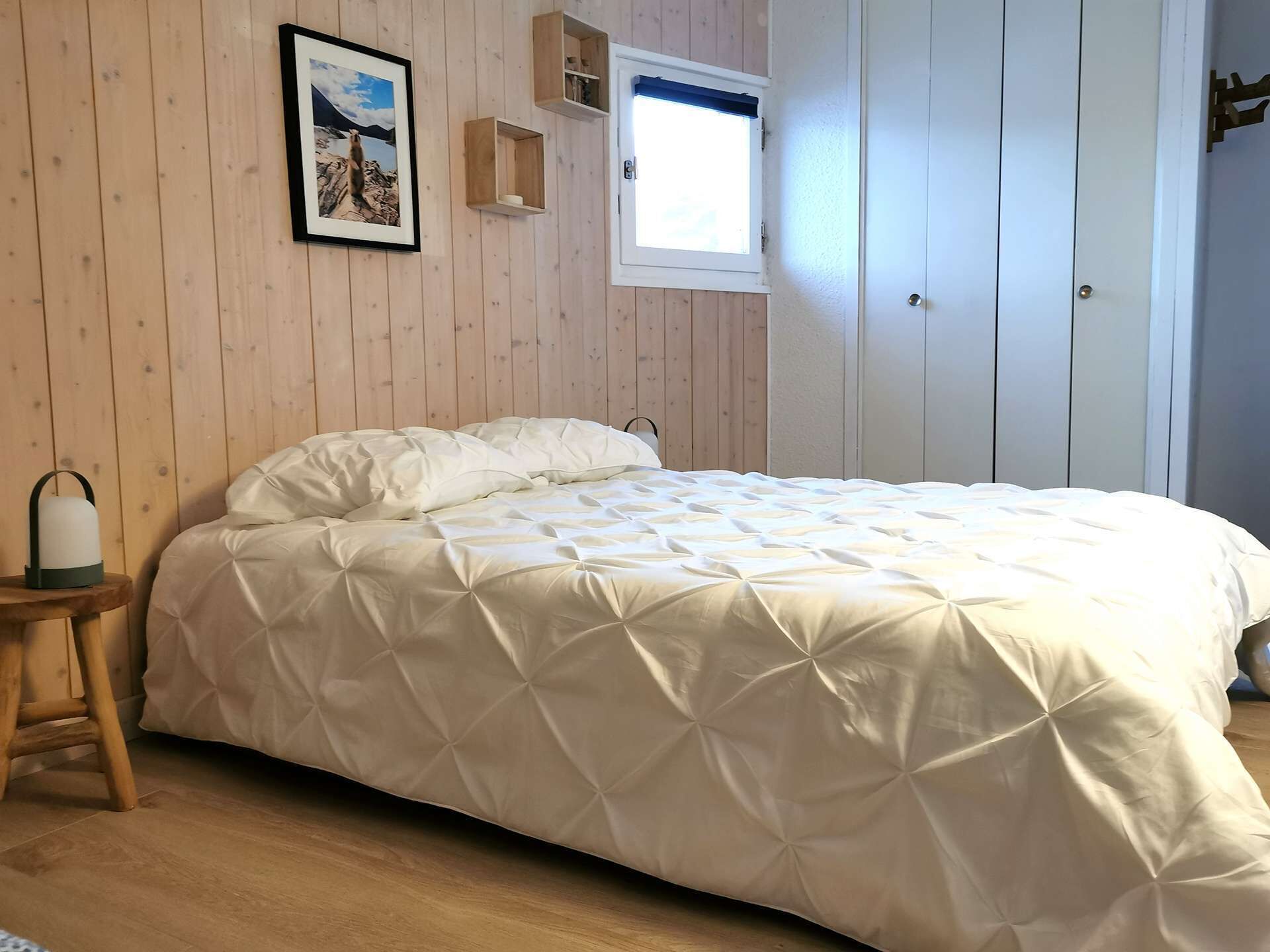 Une chambre à coucher avec un lit, des murs en bois, une fenêtre et un tableau accroché au mur.