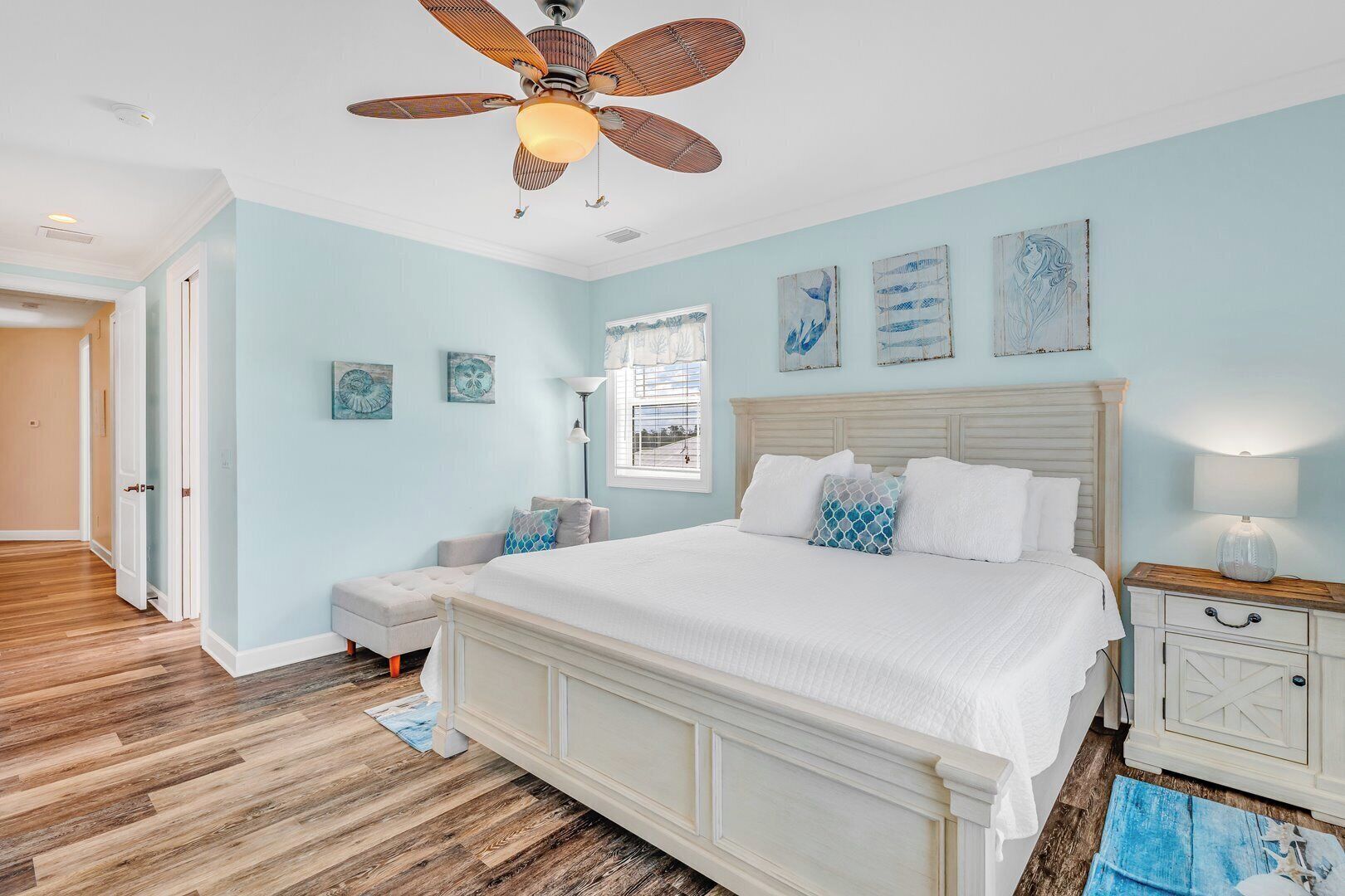 Une chambre avec un grand lit, un ventilateur de plafond et des œuvres d’art accrochées aux murs.