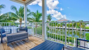A wooden deck with outdoor seating, a view of a body of water, and palm trees. - W04 - Spacious 4 bed, 3 bath home in Sombrero with private pool (Marathon)