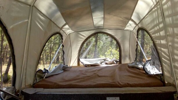 Una tienda de campaña con una cama en su interior, tres ventanas y vista a árboles.