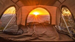 Una tienda de campaña con una cama en su interior, dos ventanas y vistas a la puesta de sol.