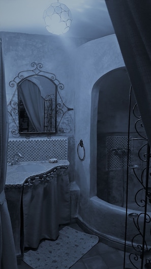 Experience the charm of this uniquely designed room with a curved wall and arched doorway, featuring a large mirror and a patterned sink countertop.