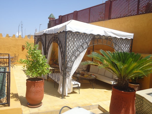 Relax on the covered terrace with a seating area, potted plants, and a small table and chairs.