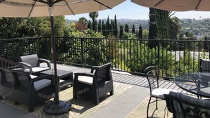 Ein Balkon mit Gartenmöbeln, darunter Korbstühle und ein Tisch, sowie zwei große Sonnenschirme, die Schatten spenden.