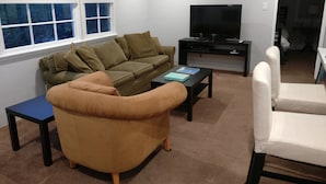 Ein Wohnzimmer mit einem braunen Sofa, einem blauen Tisch, einem weißen Sessel und einem Fernseher auf einem schwarzen Lowboard.