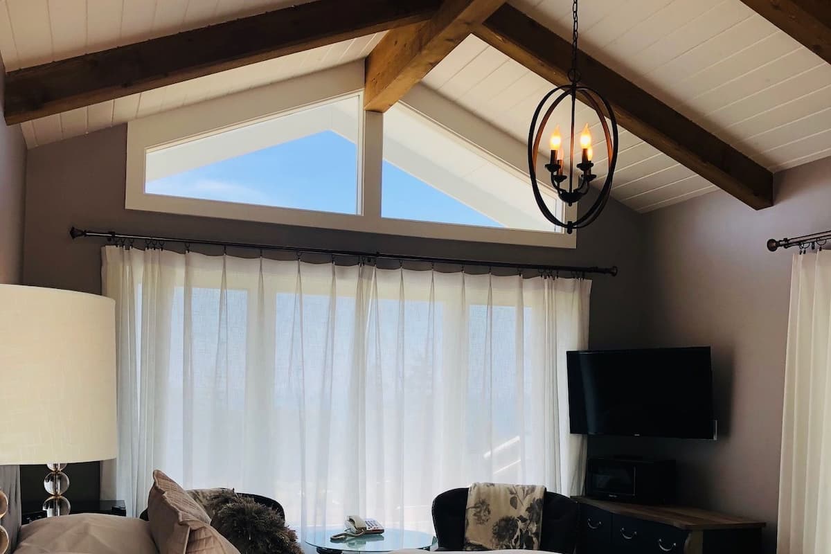 A bedroom with a large bed, a TV, a desk, and a window with curtains.