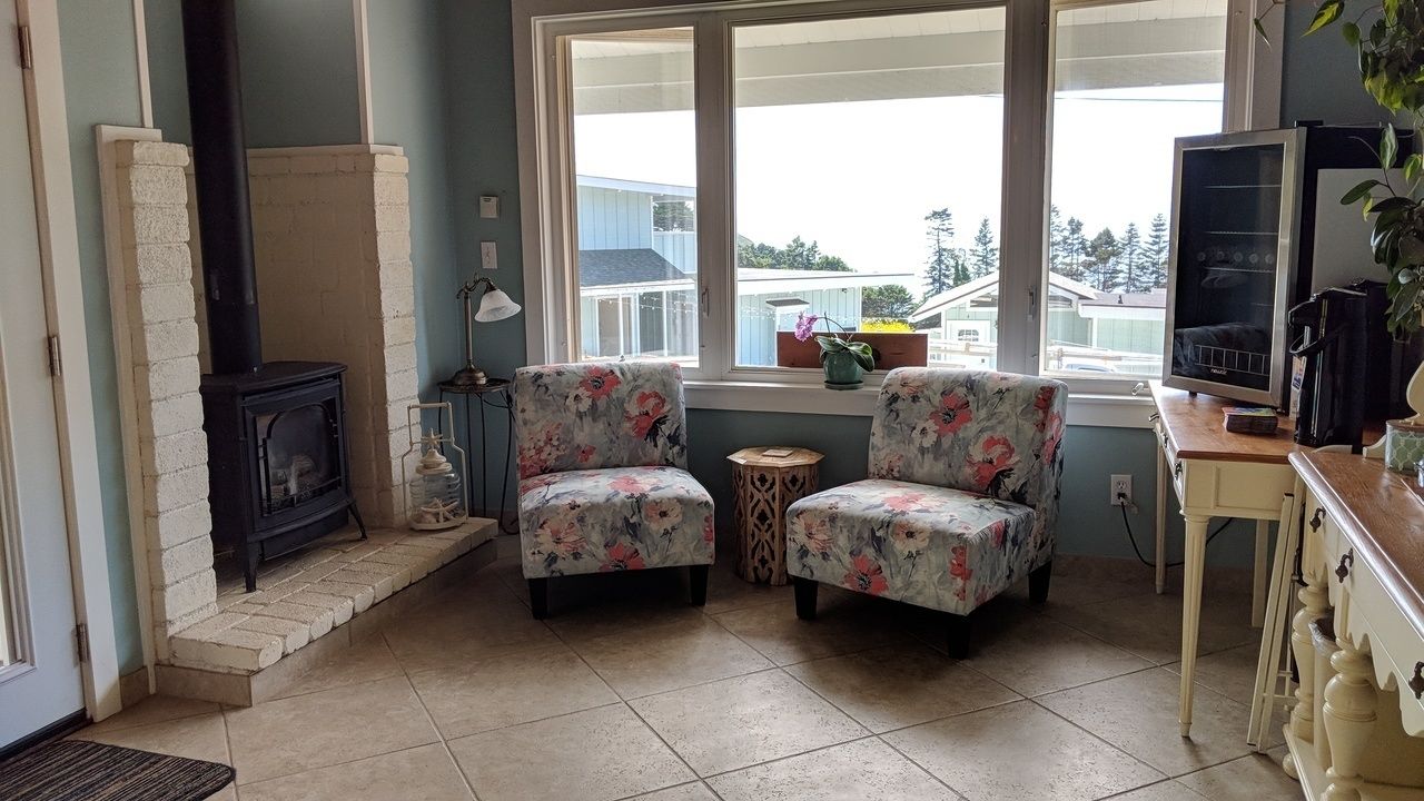A cozy living room with a fireplace, two floral armchairs, a small round table, and a television.
