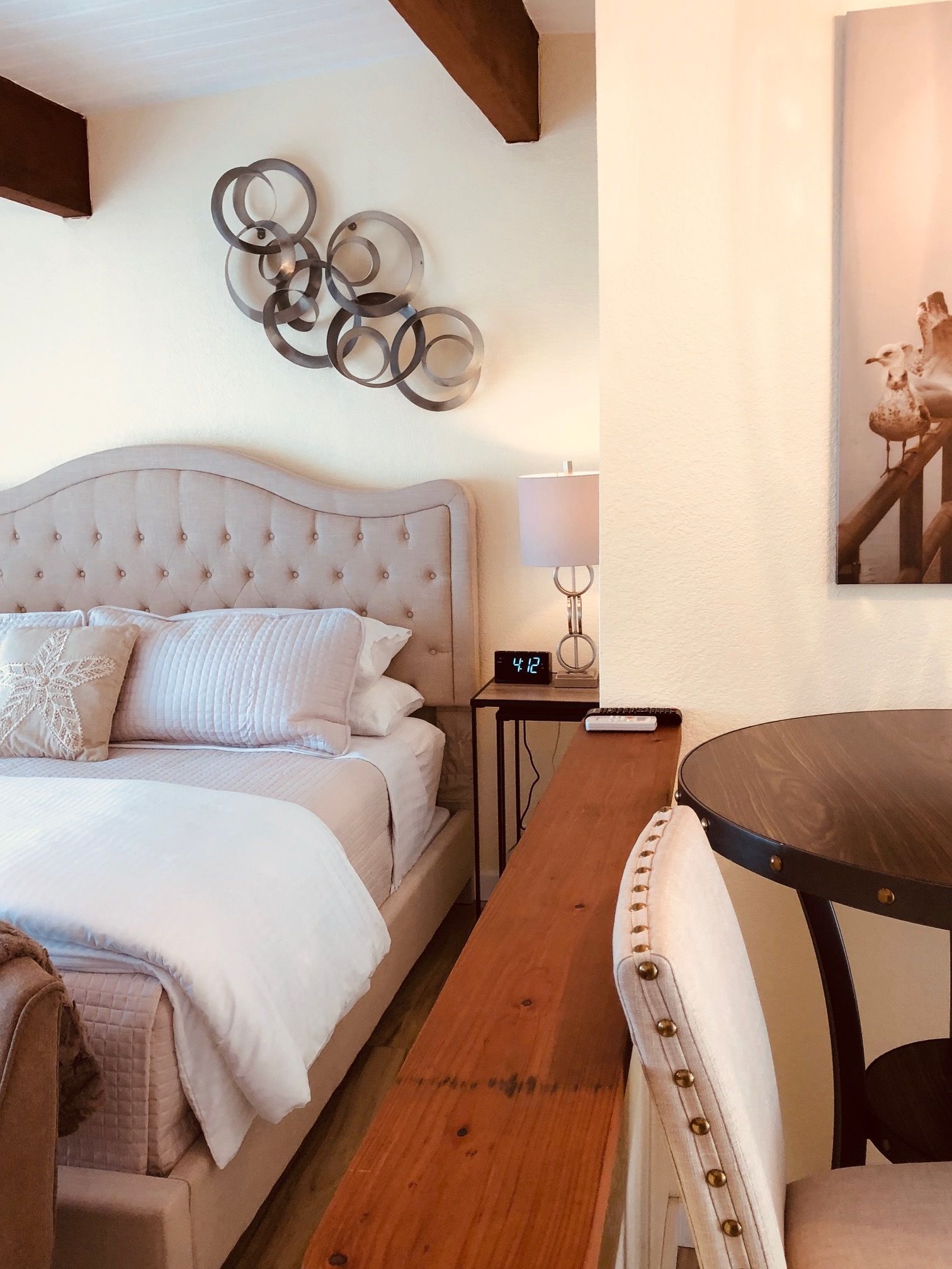 Une chambre à coucher avec une tête de lit capitonnée, une table de chevet avec une lampe, une horloge et un tableau encadr é au mur.