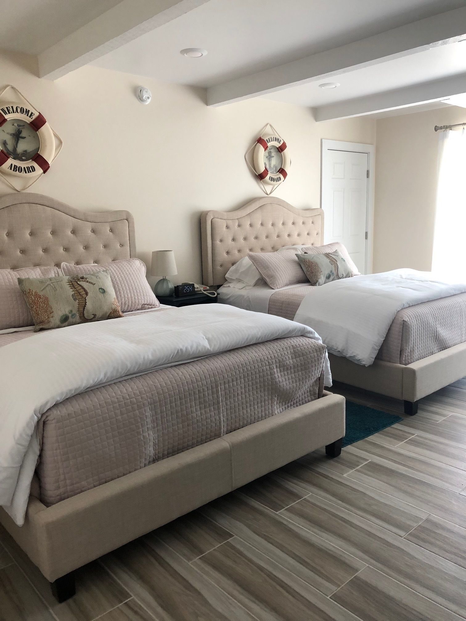 A hotel room with two beds, a clock, and a welcome sign on the wall.