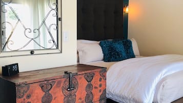 A bedroom with a wooden ceiling, a bed with white bedding, a decorative chest of drawers, and a wall-mounted light fixture.