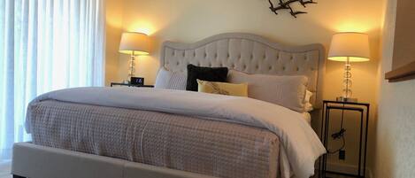 A large bed with a tufted headboard, two bedside lamps, and a wall-mounted abstract art piece.