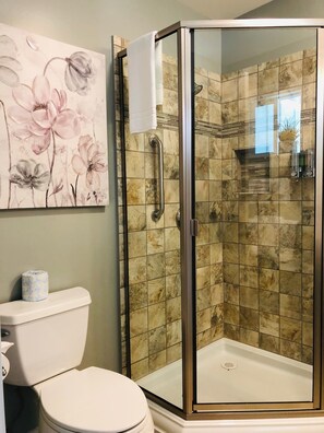 A bathroom with a glass-enclosed shower, a toilet, and a wall-mounted toilet paper holder. - Seafoam Lodge (Little River)