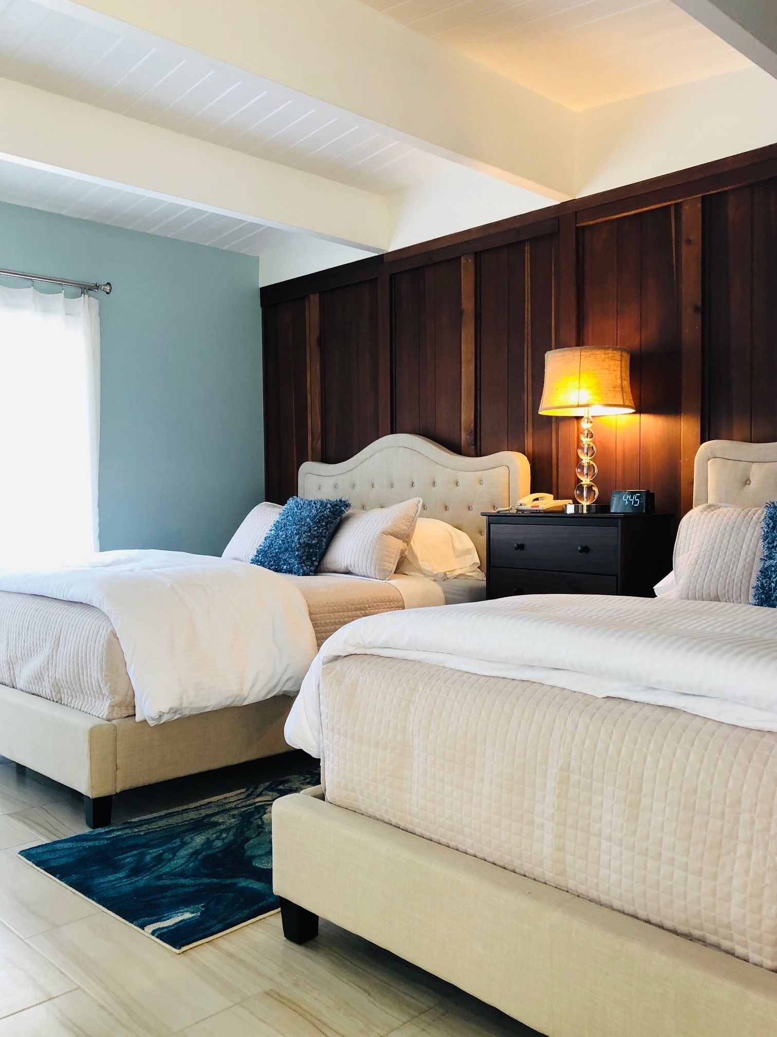 A bedroom with two beds, a nightstand with a lamp, and a wooden headboard.