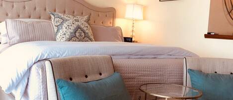 A bedroom with a large bed, a bedside table, a chair, and a small round table.