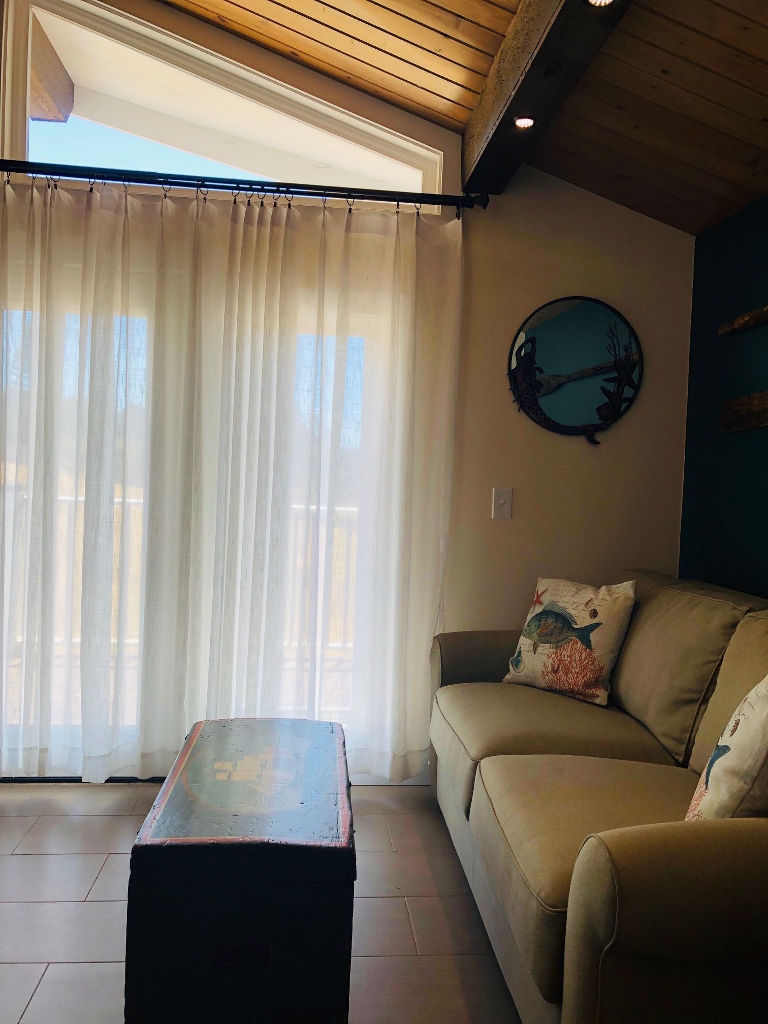 A living room with a sofa, a coffee table, and a large window with sheer curtains.