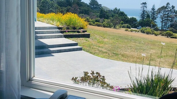 Una habitación con vistas a un jardín ajardinado y al océano.