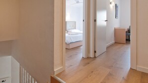 Un corridoio con pavimento in legno che conduce a una camera da letto con un letto e un comodino.