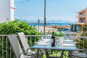 An outdoor table with chairs, a bottle of wine, and a vase of flowers, overlooking a beach with umbrellas and people. - Duplex Apartment with WIFI, AC and garden in front of the beach, Port d'Alcudia. (Alcúdia)