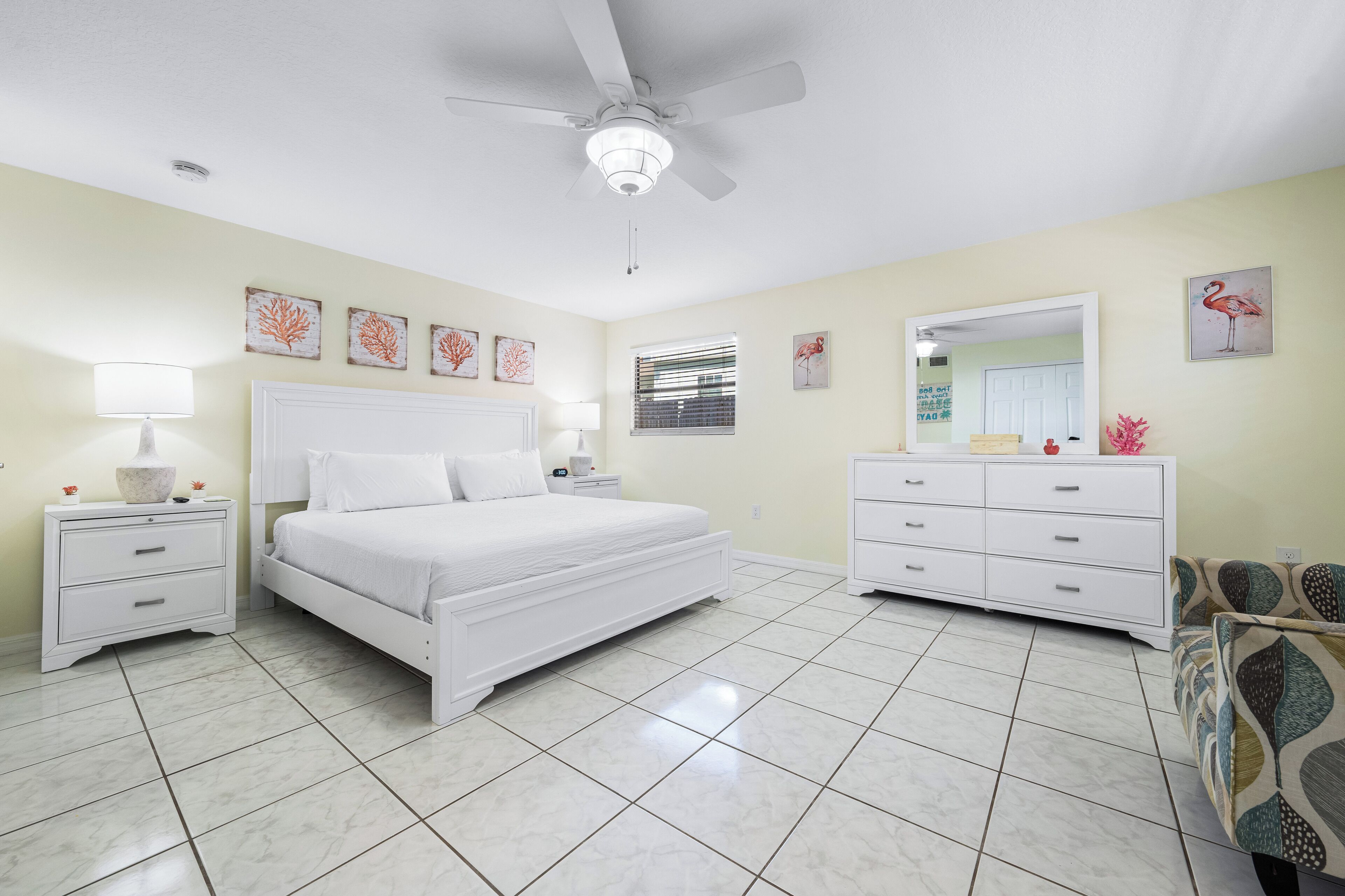 Un dormitorio con cama, mesitas de noche, cómoda, ventilador de techo y decoración en las paredes.