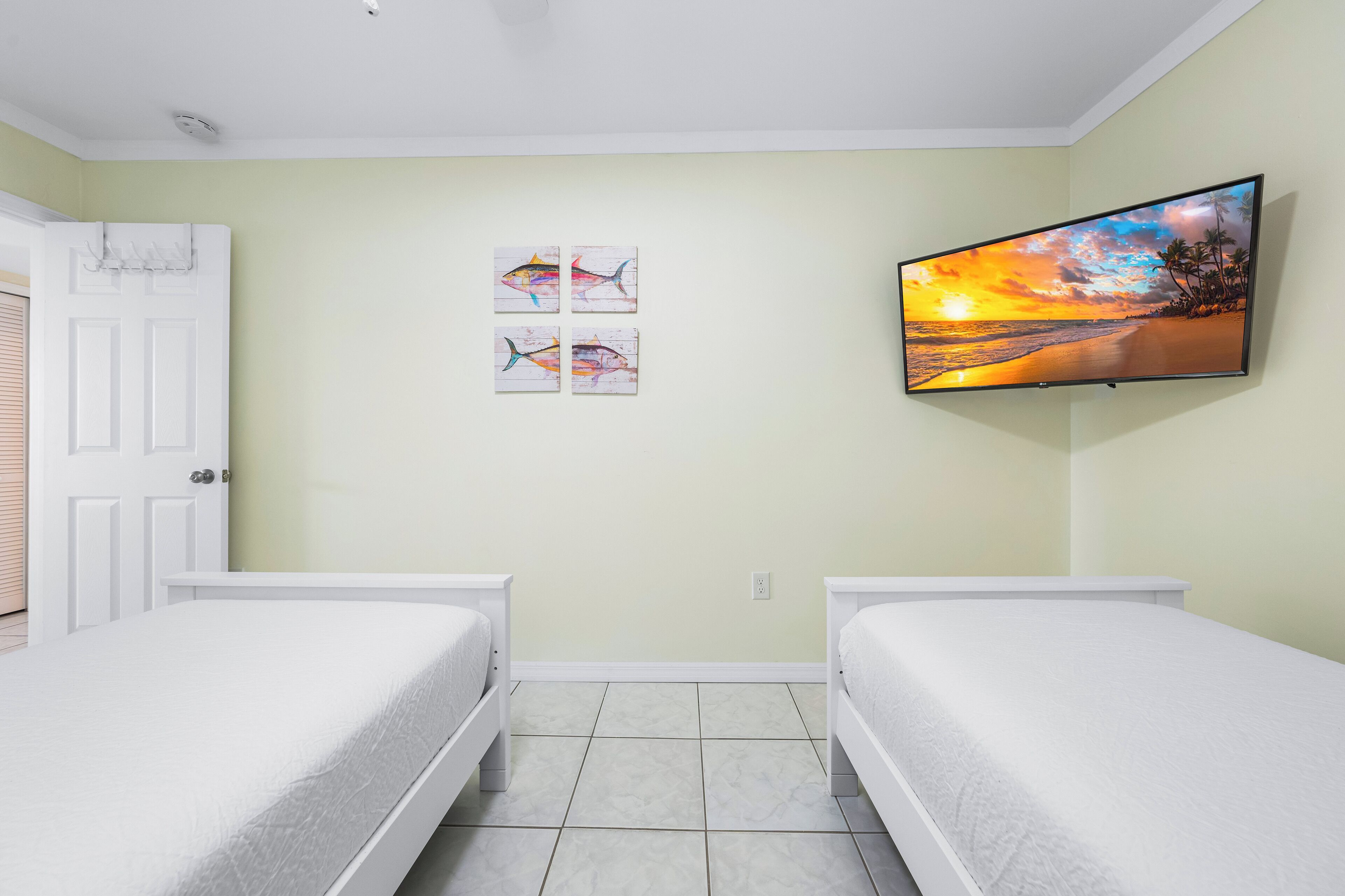 A bedroom with two beds, a TV mounted on the wall, and artwork above the beds.