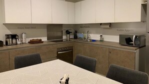 Cozinha moderna com armários brancos, uma mesa de jantar com cadeiras e uma máquina de café.