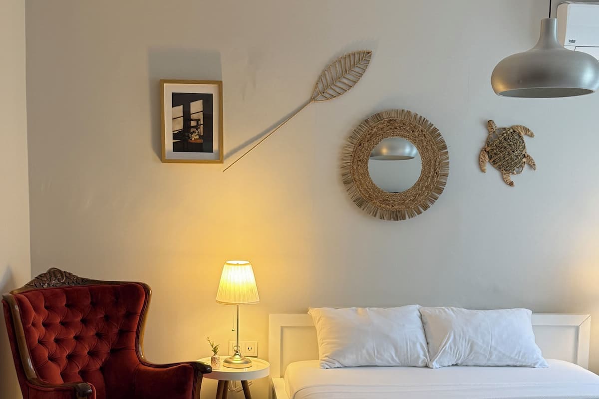 A bedroom with a bed, a red armchair, a small table with a lamp, and wall decorations including a leaf and a turtle.