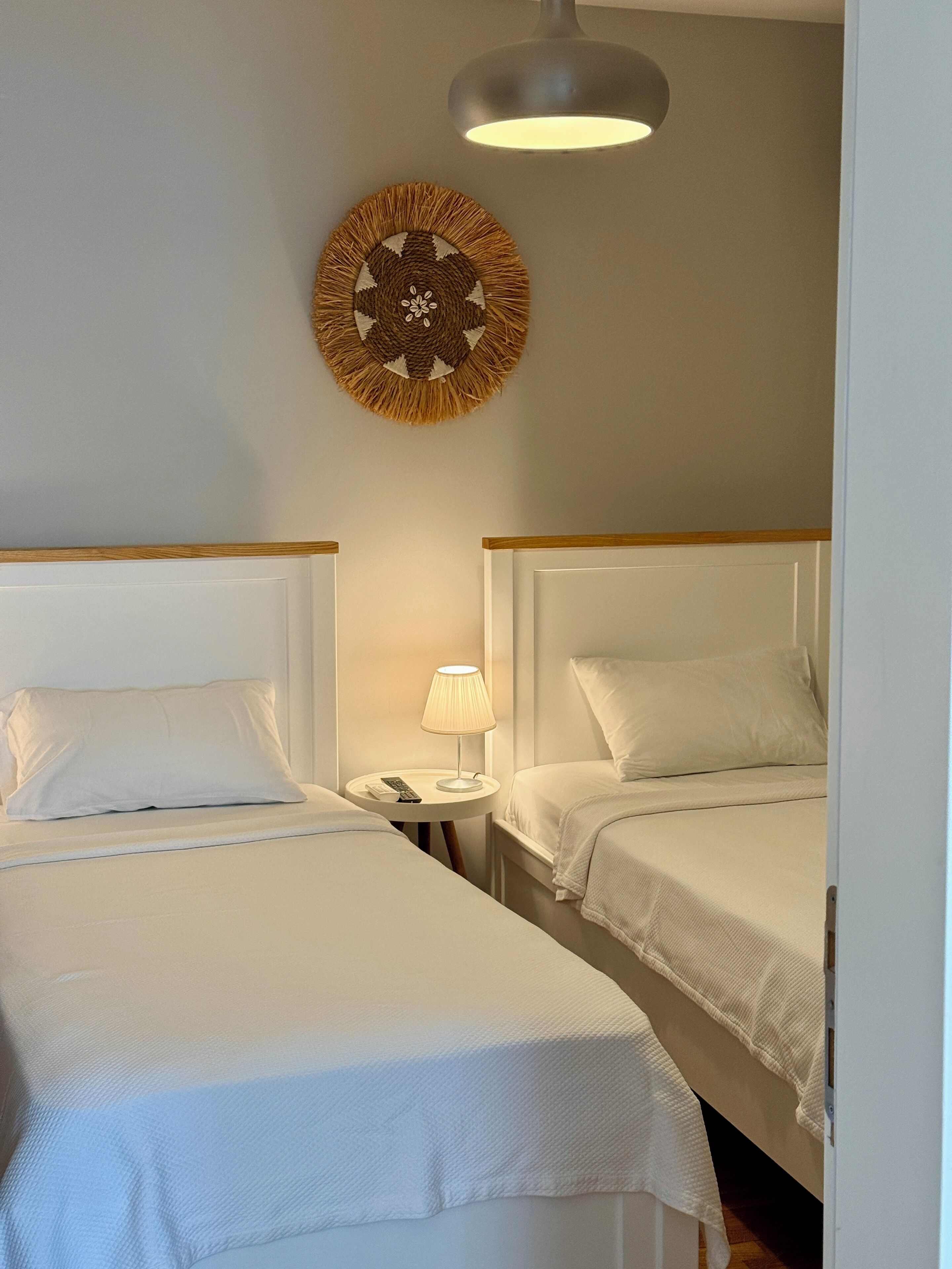 Una habitación de hotel con dos camas, una mesita de noche con lámpara y un cuadro en la pared.