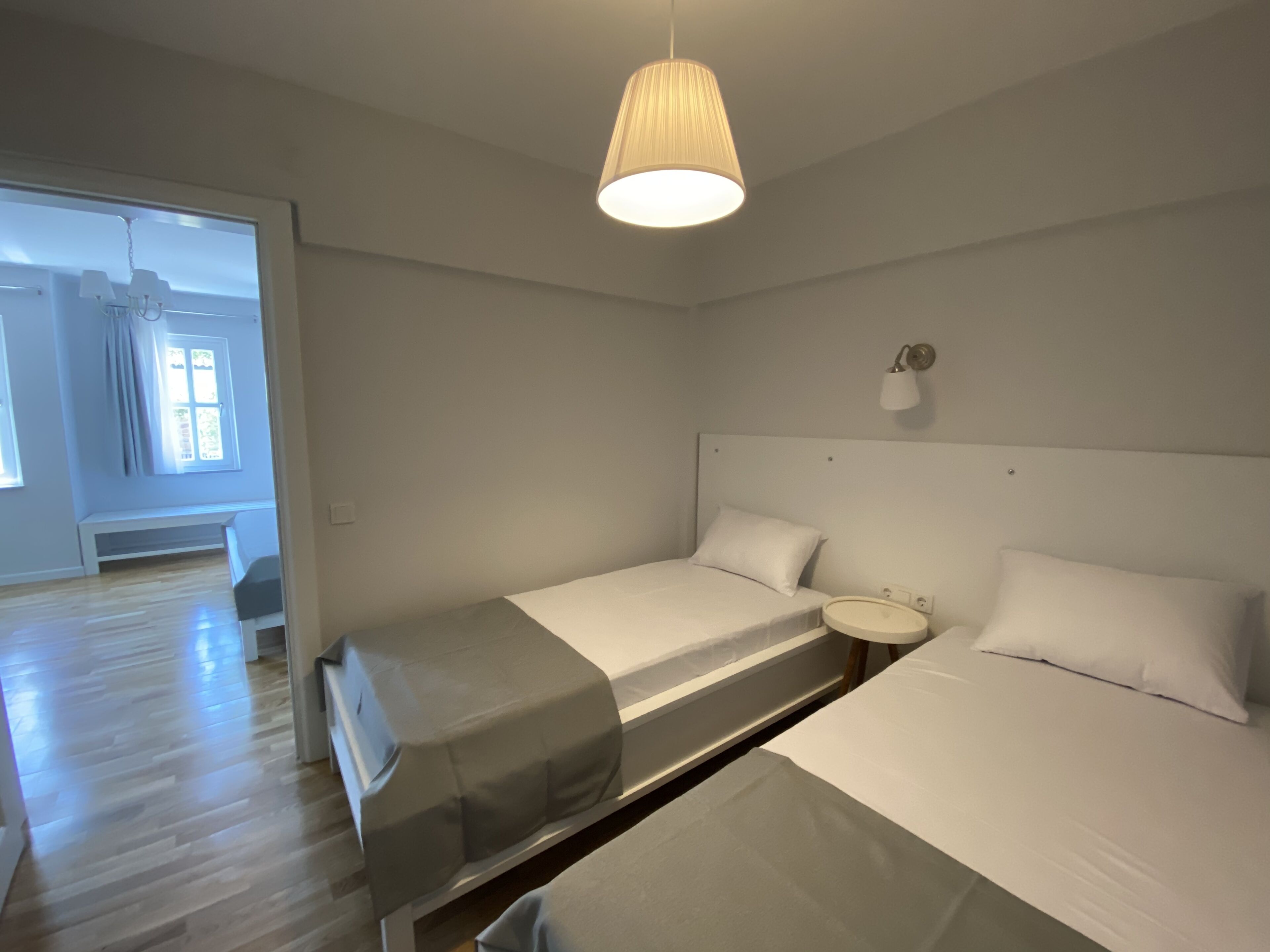 Habitación de hotel con dos camas, una mesita de noche, una lámpara y una ventana con cortinas.