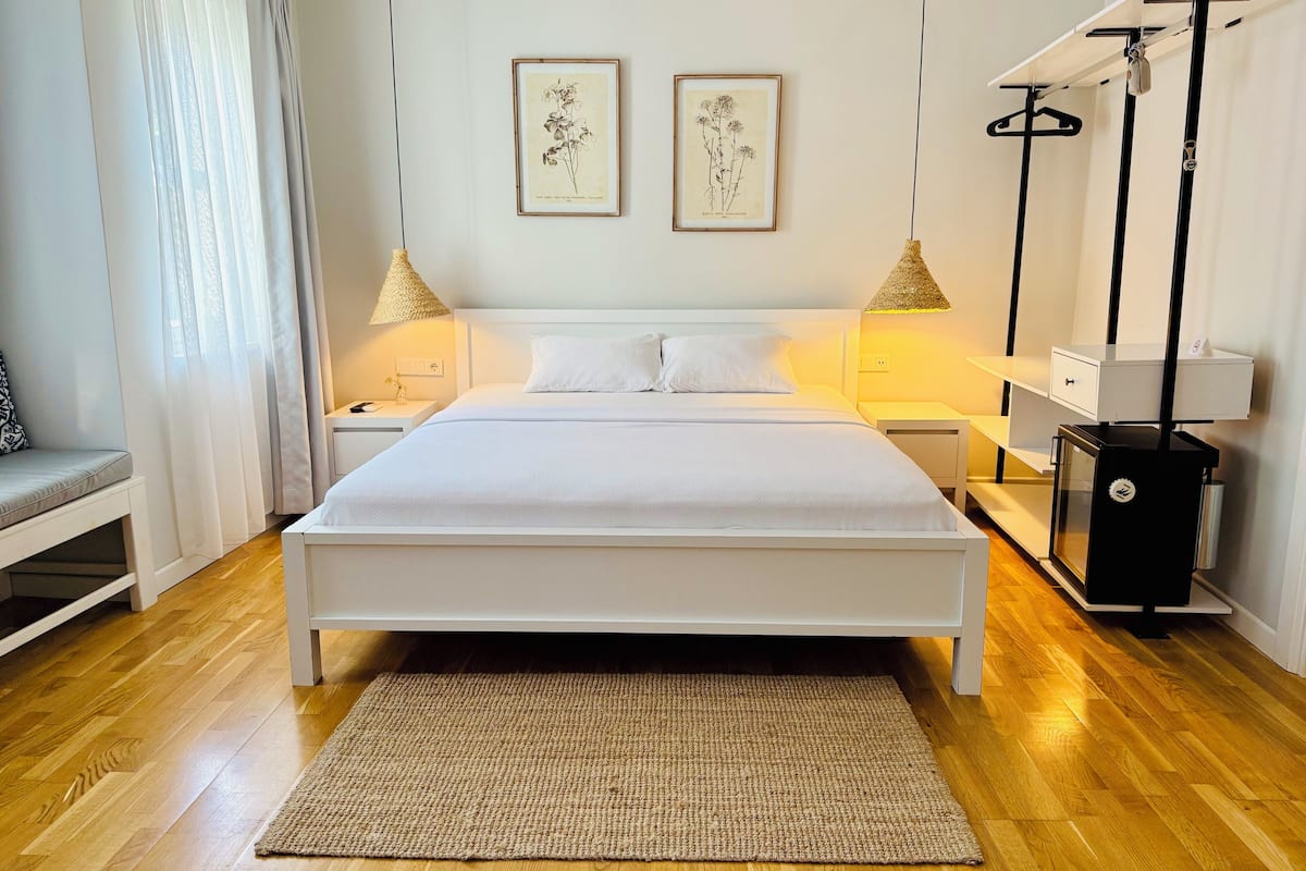 A bedroom with a large bed, two bedside tables, a bedside lamp, a hanging light fixture, a small cabinet, and a radiator.