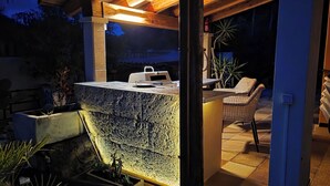 Zona de pati exterior amb un taulell de pedra, una barbacoa i una cadira.