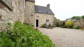 A stone building with a gravel driveway, a small garden, and a table with chairs.