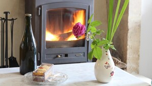 A cozy room with a wood-burning stove, a vase with a rose, and a loaf of bread on a table.