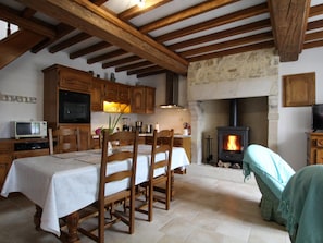Une cuisine rustique avec des poutres en bois, une cheminée en pierre et un coin repas comprenant une table et des chaises.