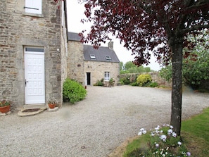 Un bâtiment en pierre avec une allée en gravier, une porte blanche et des plantes en pot.