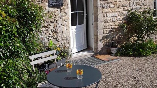 A stone building with a white door, a small outdoor table with two glasses, and a bench.