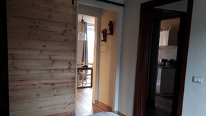 Un dormitori amb una paret de fusta, un llit amb un estovat estampat i vista a una zona de menjador amb una taula i cadires.