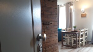 Una habitació amb una porta de fusta, una zona de menjador amb taula i cadires, i un llum penjant.