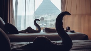 Cama com travesseiro e fronha em formato de cisne, vista para a pirâmide.