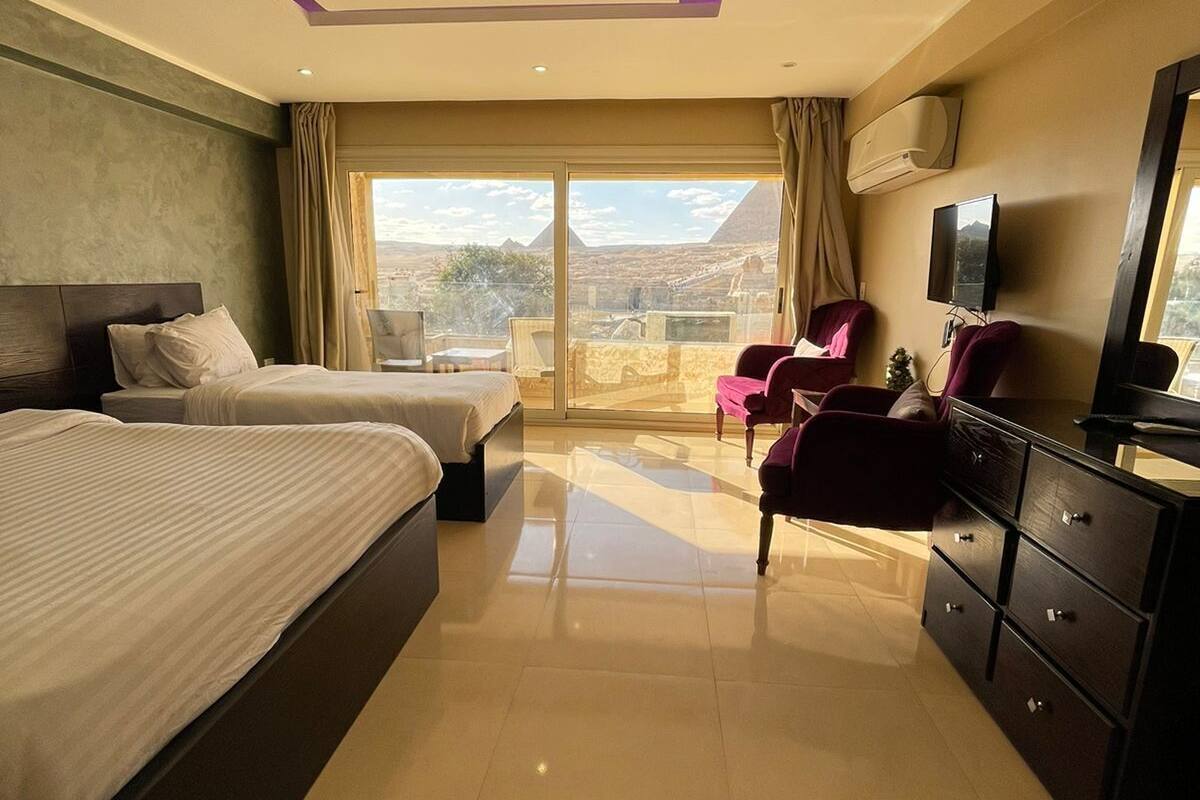 A hotel room with two beds, a TV, a dresser, and a balcony with a view of the mountains.