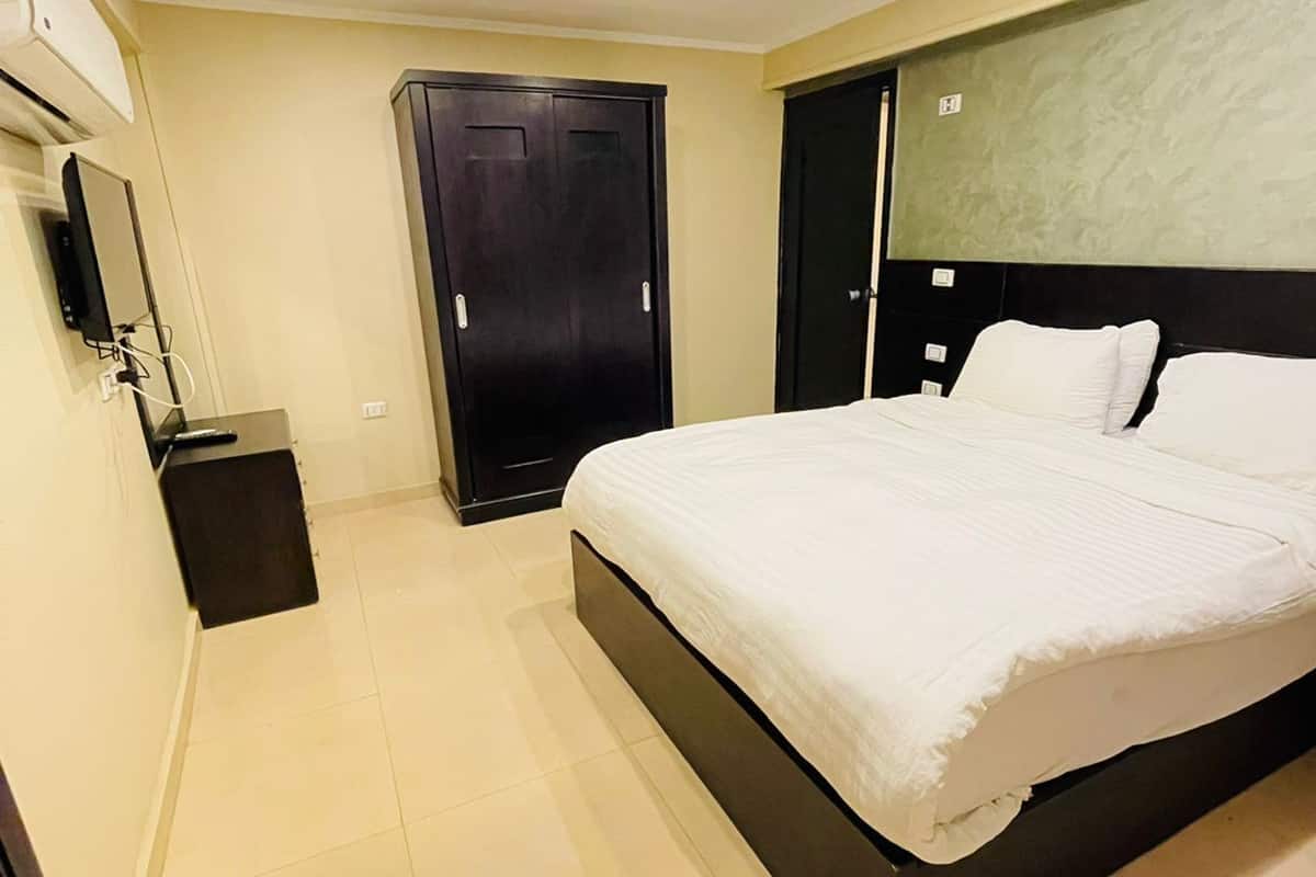 A hotel room with a large bed, a wardrobe, a mirror, and a small desk.