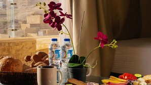 Mesa de jantar com alimentos, garrafas de água e uma orquídea em vaso. Uma janela mostra vista de uma pirâmide.