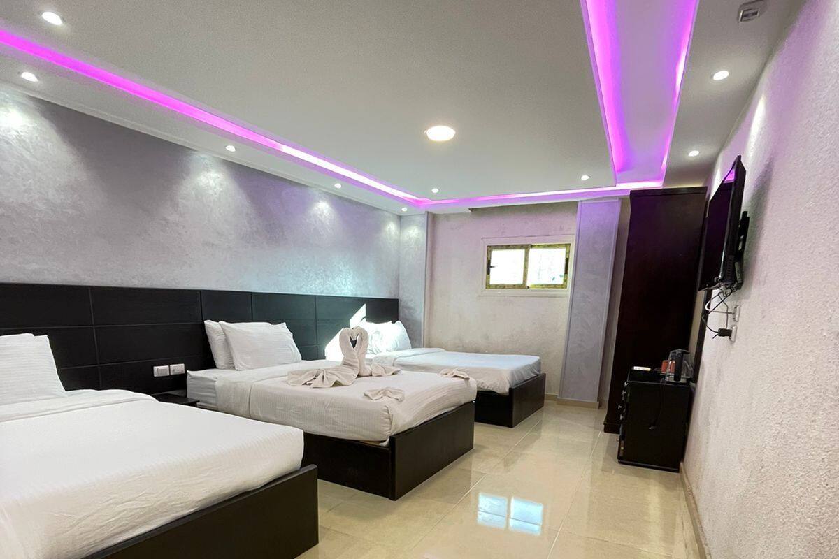 A hotel room with three beds, a flat-screen TV, and a minibar.