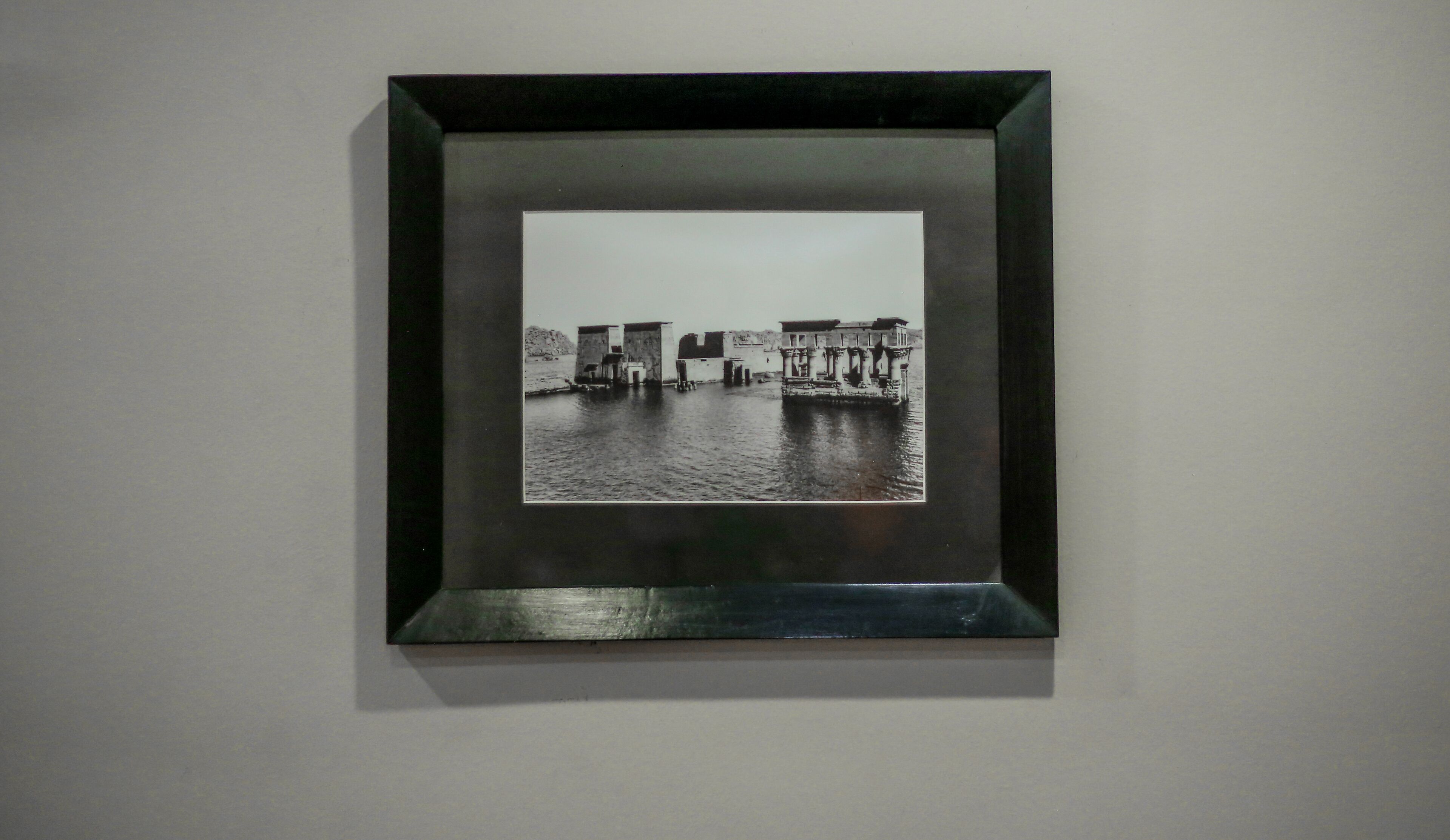A framed black and white photograph of a waterfront scene with buildings and water.