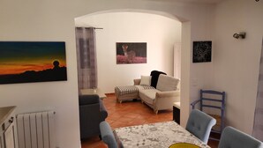 A dining area with a table set for four, a sofa, and a chair. There are two paintings on the wall, a radiator, and a window with a curtain. - Villa at the foot of Mont Ventoux for 7 people in Malaucène with private pool (Malaucène)