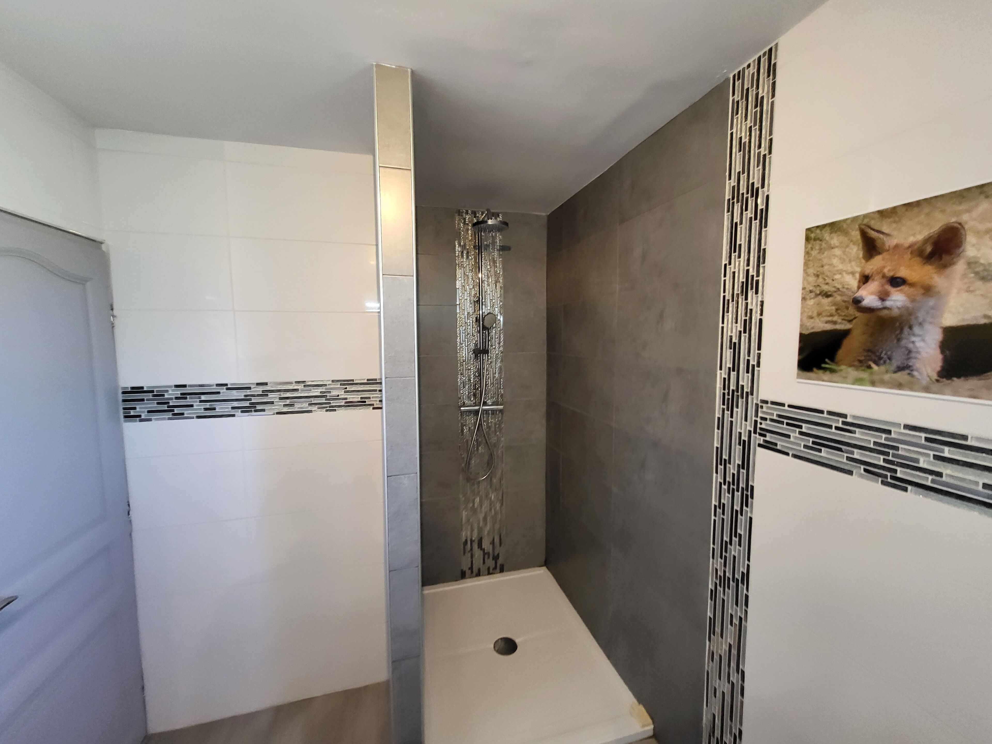 Une salle de bain avec douche, murs carrelés et panneau décoratif mural.