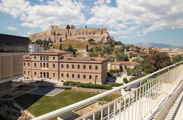 A historical building with a courtyard, a view of a hilltop fortress, and a modern structure in the foreground.