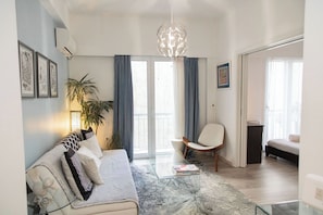 Un salon moderne avec un canapé, une table basse, un fauteuil et une grande fenêtre avec des rideaux.