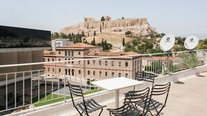 A terrace with a table and chairs overlooking ancient ruins and a modern building. - Philoxenia Flat (Athina)
